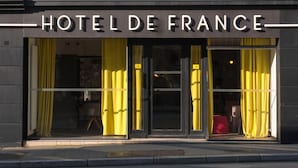 The exterior of Hotel De France with large glass doors and yellow curtains. - Urban Style Hotel de France (Vannes)