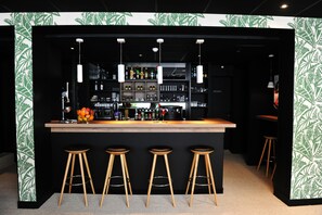 A bar area with a wooden counter, three stools, and shelves stocked with bottles and glasses. - Urban Style Hotel de France (Vannes)