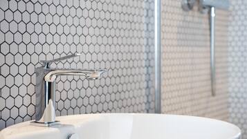 Ein Badezimmer mit weißem Waschbecken, Armatur aus Chrom und einer Duschkabine mit Glastür.
