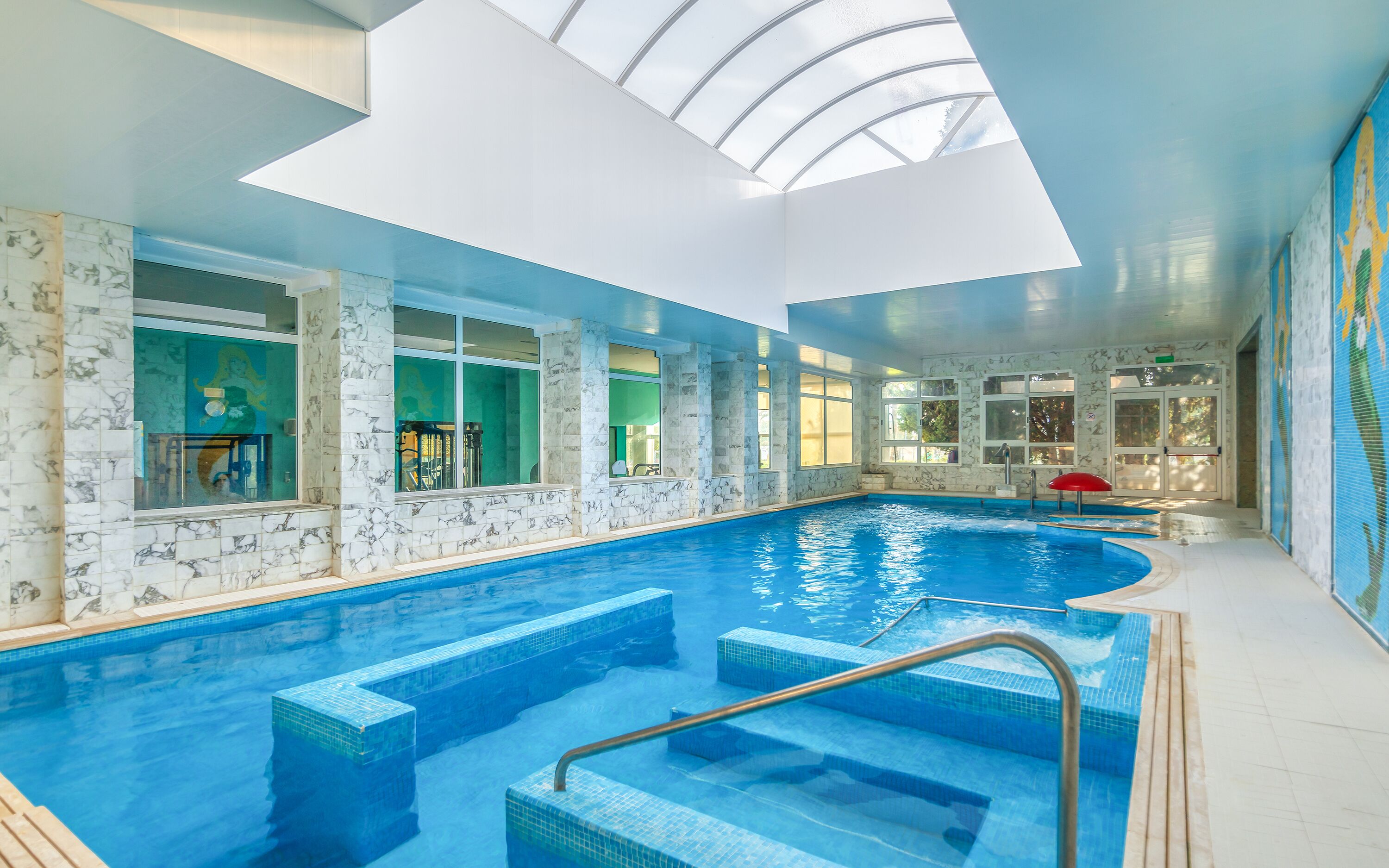 An indoor swimming pool with clear blue water, marble walls, and a skylight above.