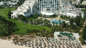 Eine Luftaufnahme eines Resorts mit einem großen Gebäude, einem Strand mit vielen Sonnenschirmen und einem Pool.