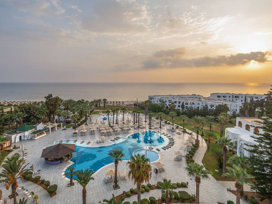 A resort with a large pool, palm trees, and a view of the sea.
