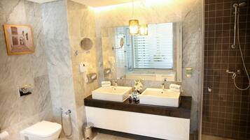 Une salle de bain avec deux lavabos, des toilettes, une douche et un mur en marbre.