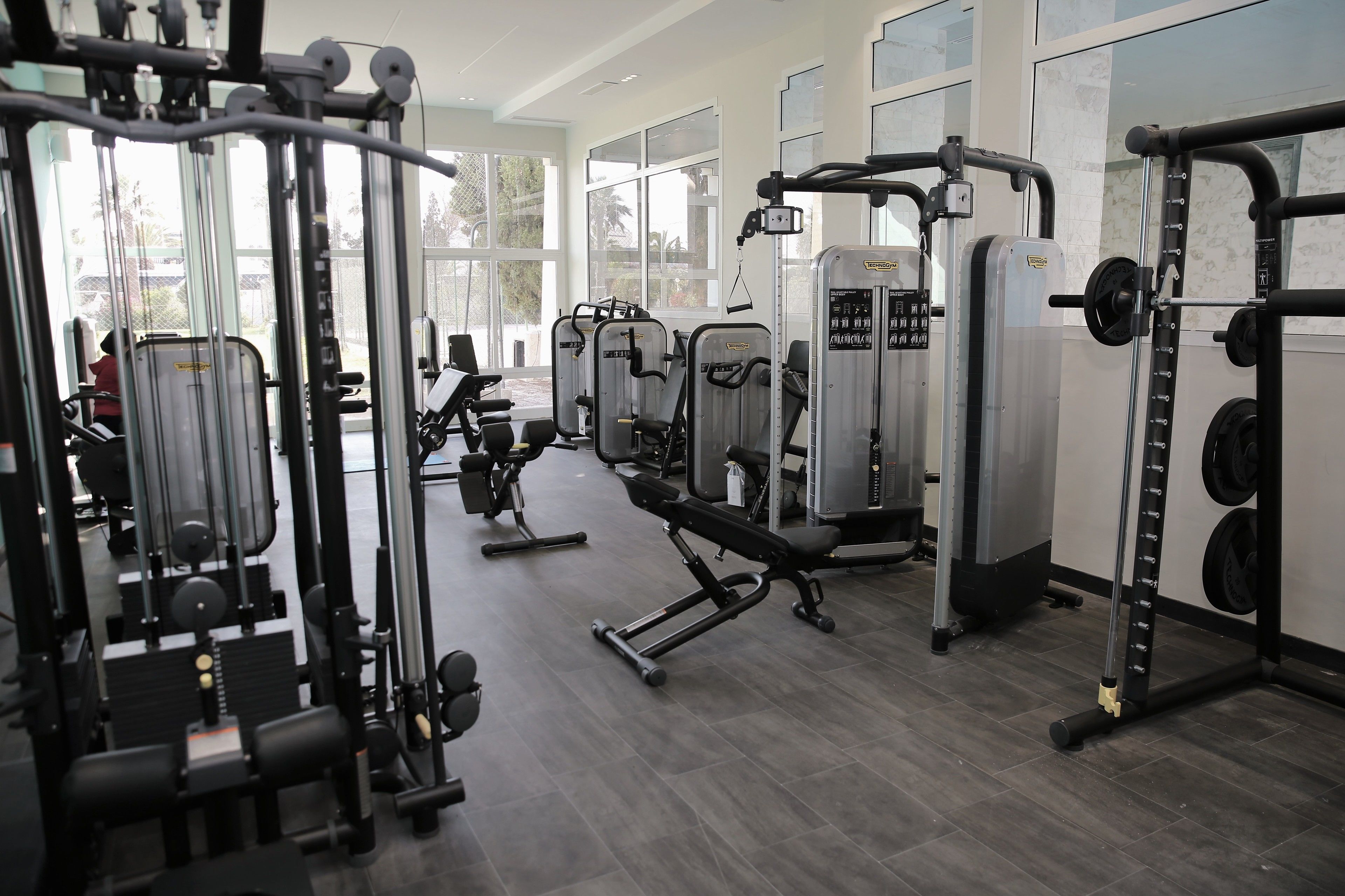 A gym with various exercise machines, large windows, and a clean, modern design.