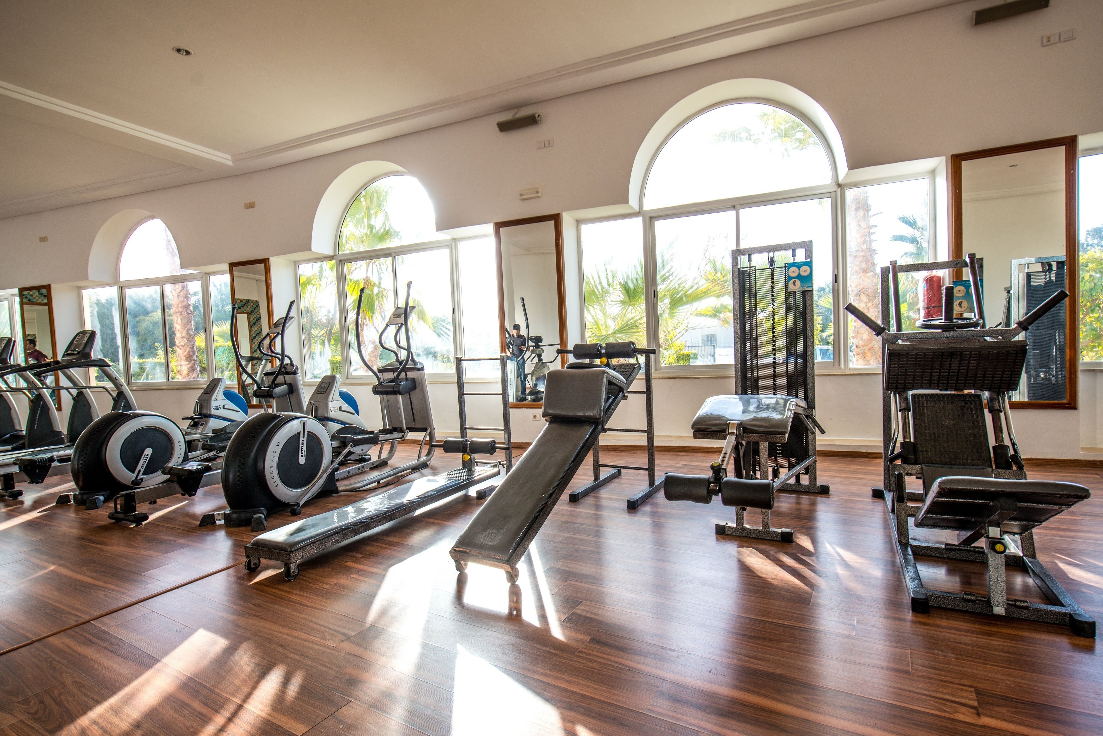 Un gimnasio con diverso equipo de ejercicio, amplias ventanas y suelo de madera.