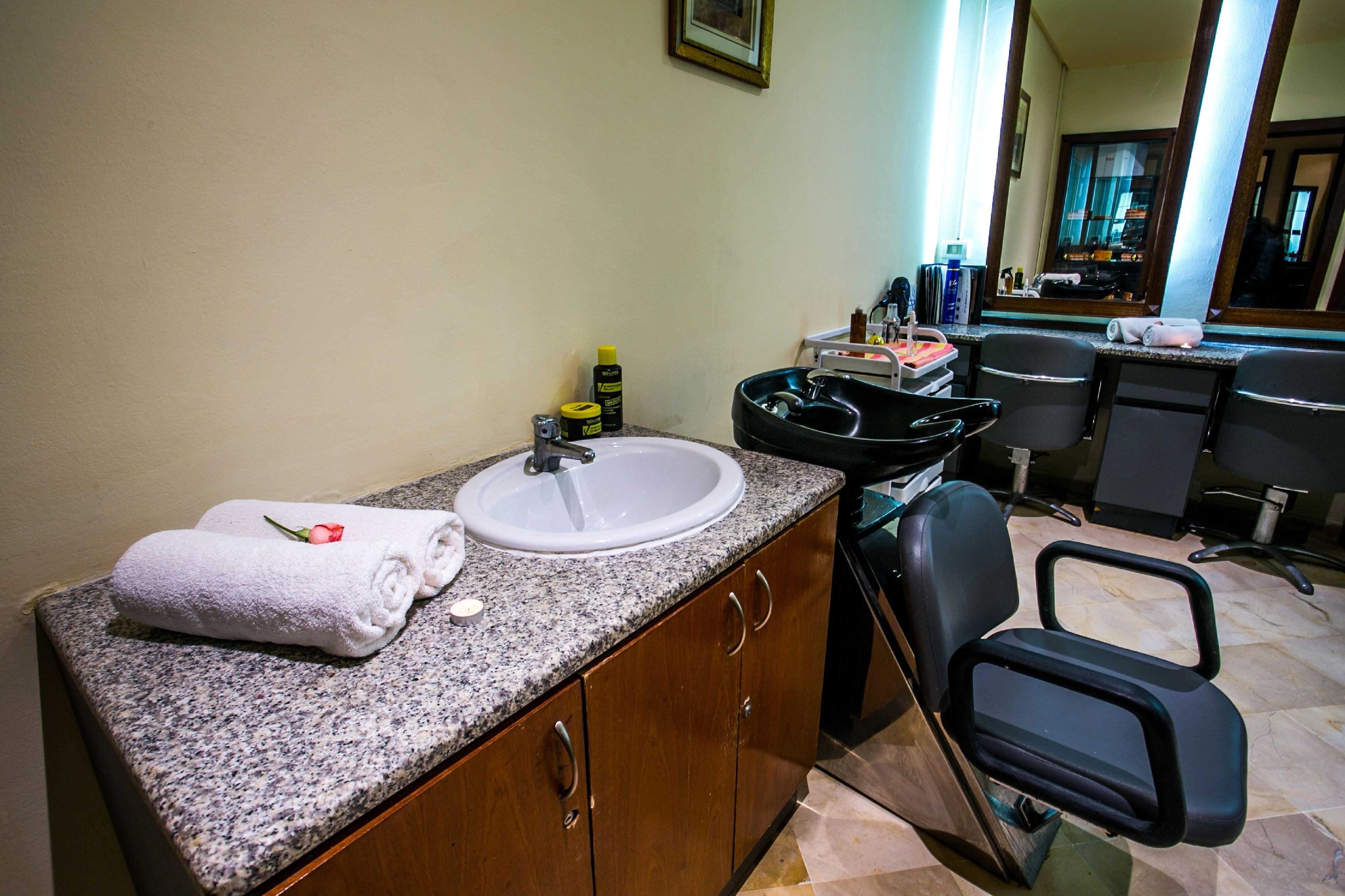 Un baño con encimera de granito, un lavabo blanco, una silla negra y un espejo.
