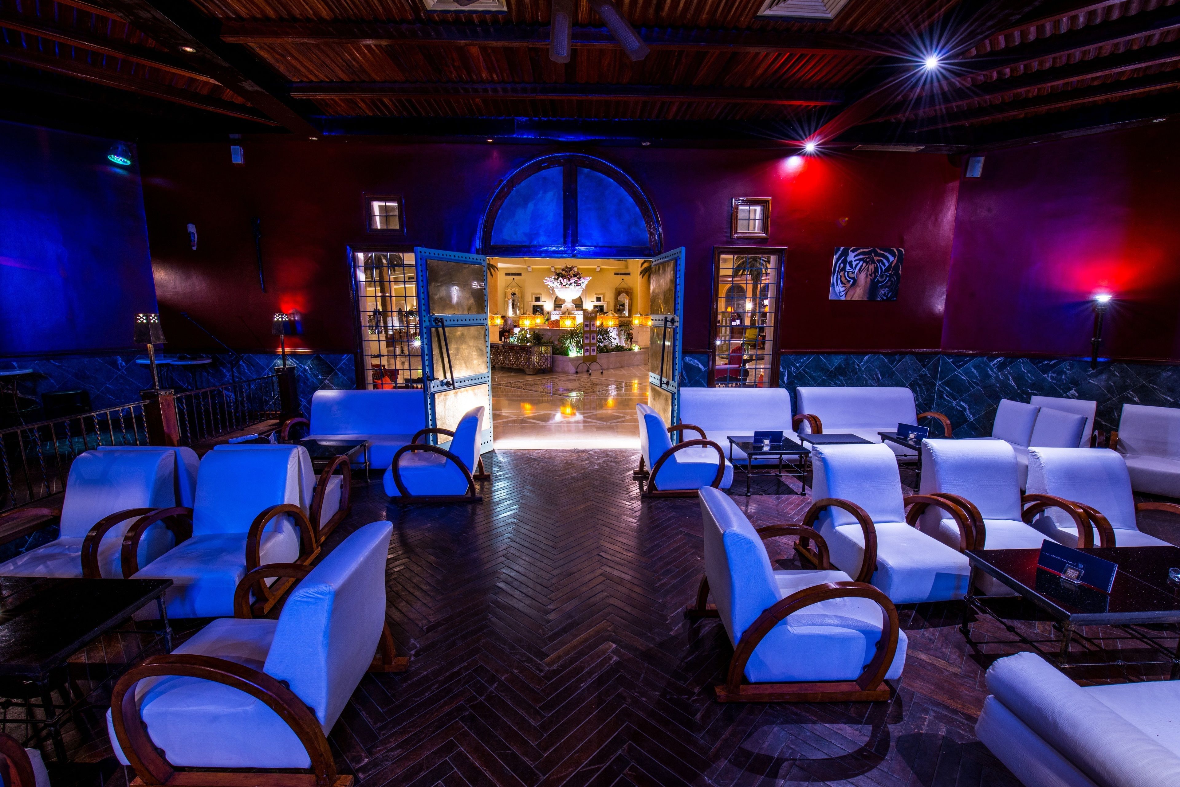 A lobby with a herringbone floor, white leather sofas, and wooden chairs.