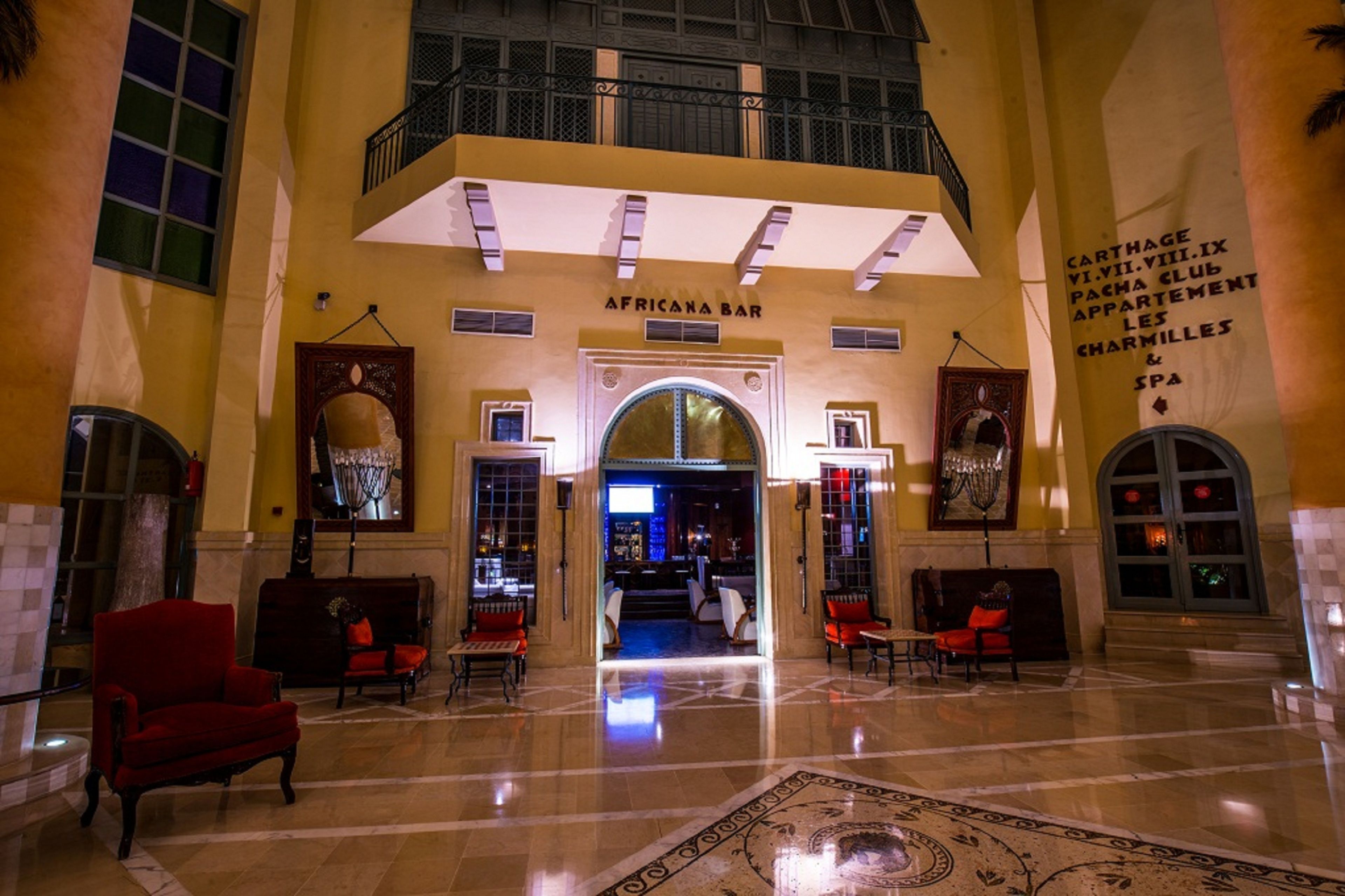 A spacious lobby with a high ceiling, a central staircase, and a bar named 'AFRICANA BAR'.