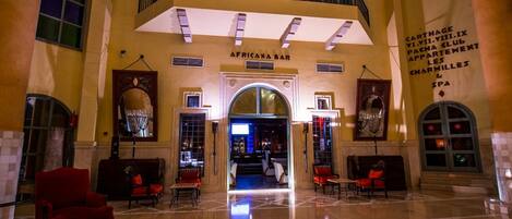 A spacious lobby with a high ceiling, a central staircase, and a bar named 'AFRICANA BAR'.