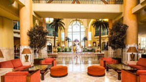 A spacious lobby with a high ceiling, a central fountain, and seating areas with orange sofas and ottomans. - Carthage Thalasso Resort (La Marsa)