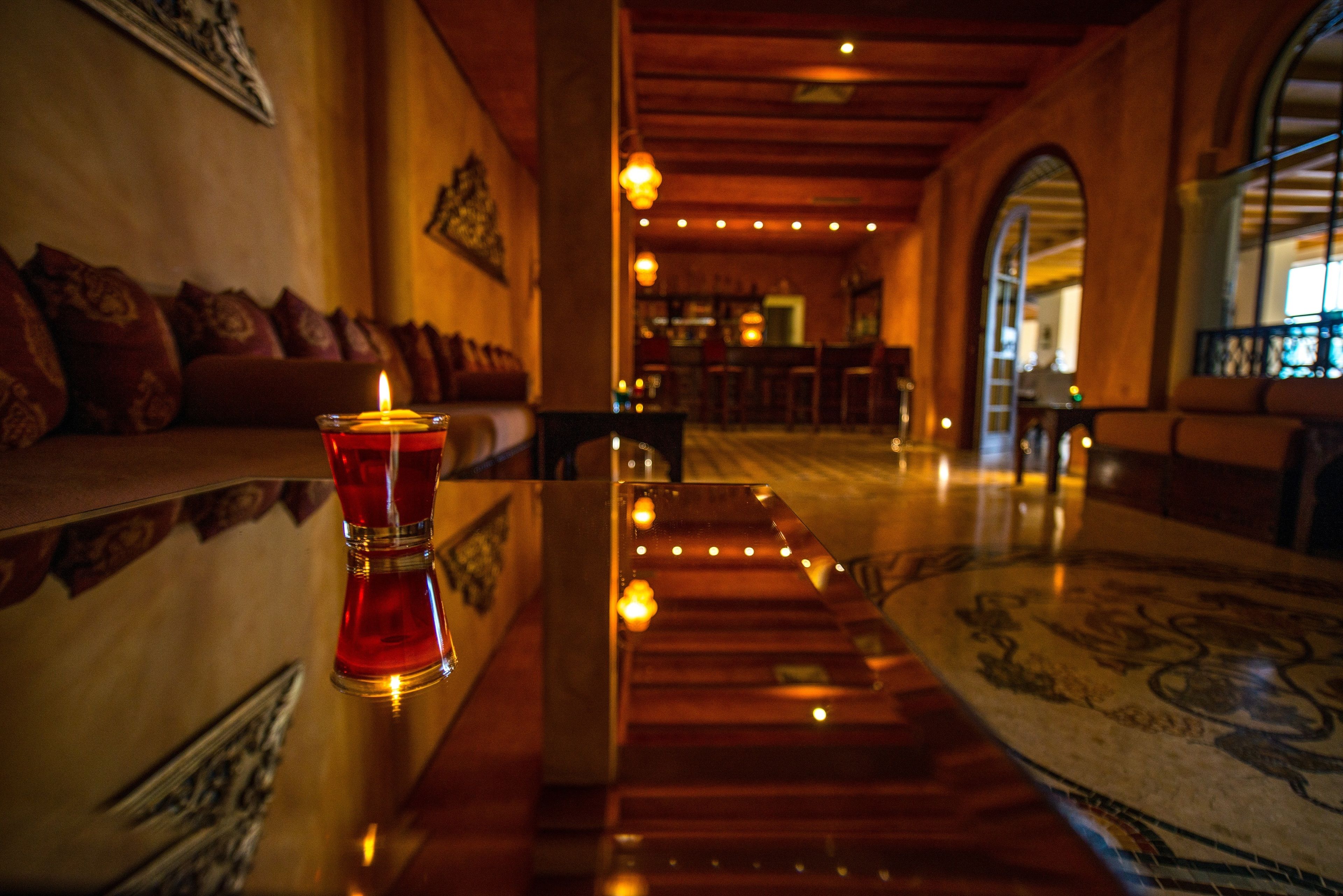 A dimly lit hallway with a candle on a table, wooden benches, and a patterned carpet.