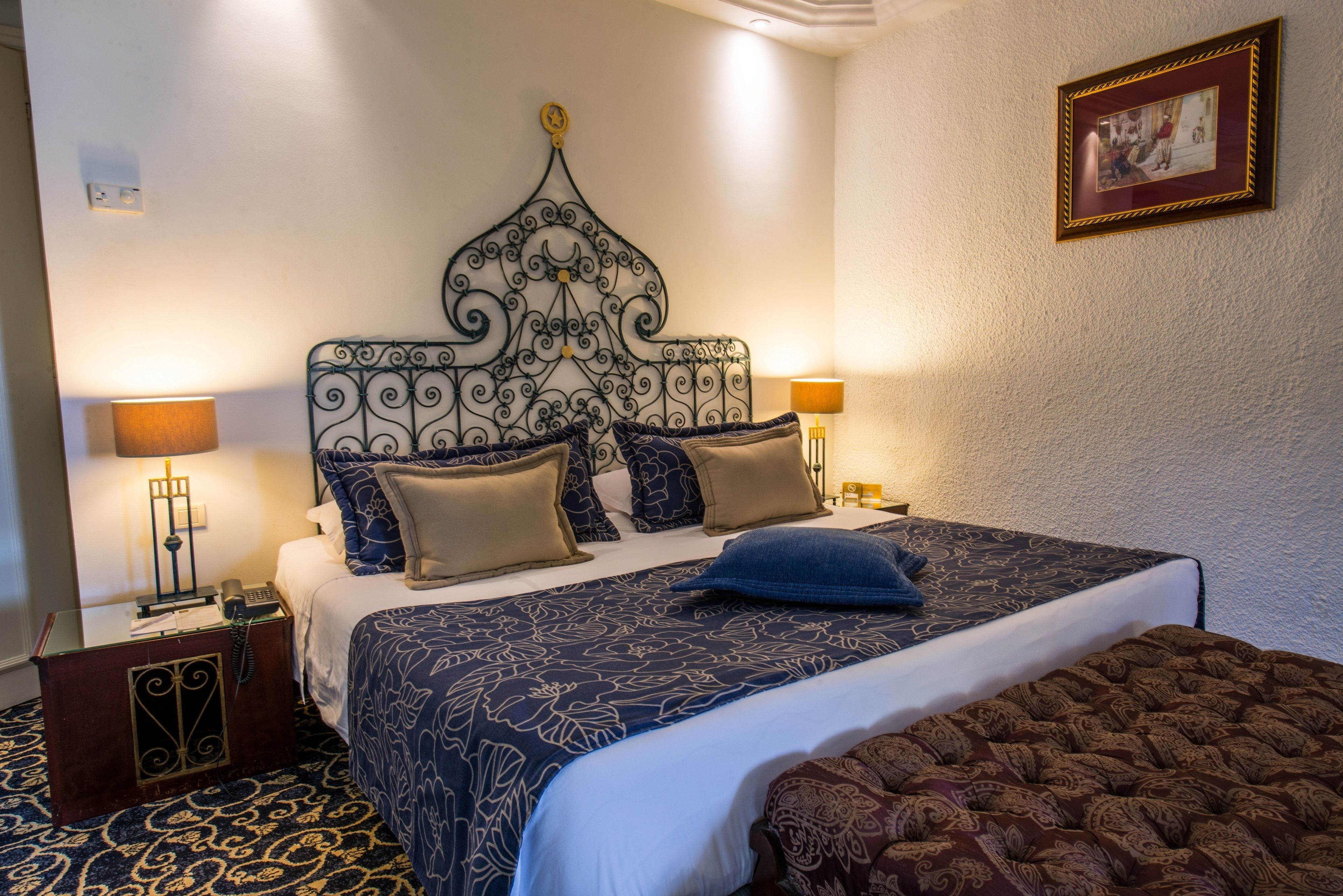 A neatly made bed with a patterned bedspread, two bedside lamps, and a decorative headboard.