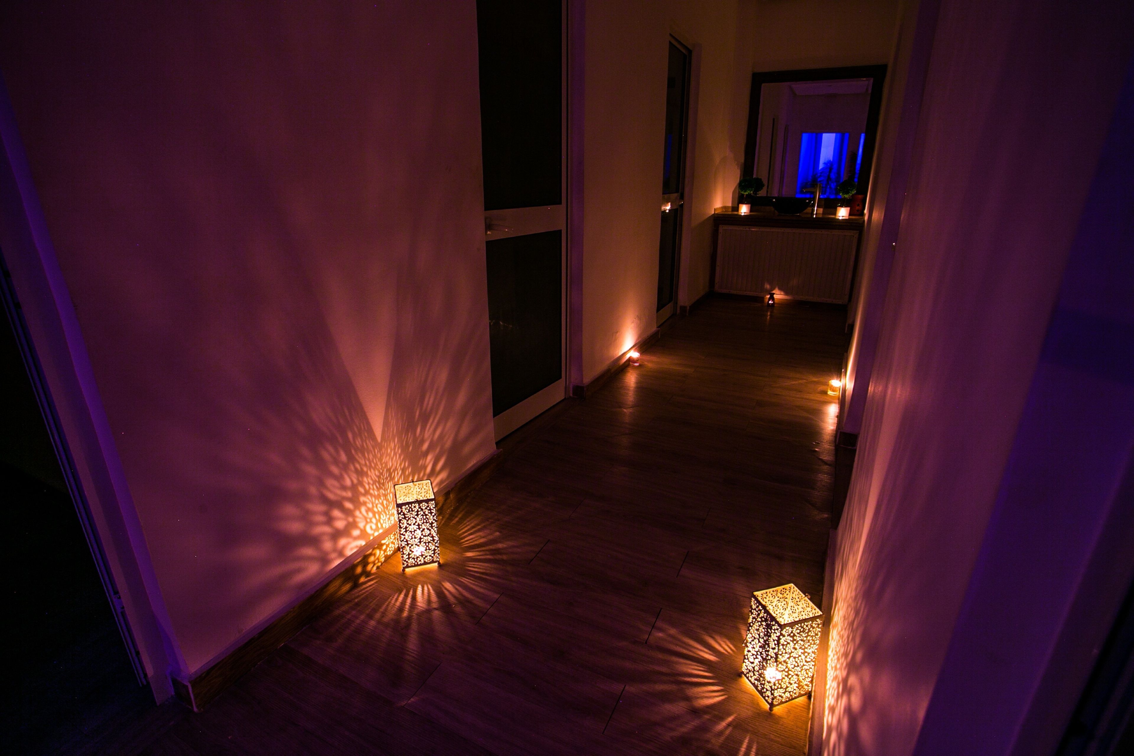 A hallway with wooden flooring and walls, illuminated by small square lanterns.