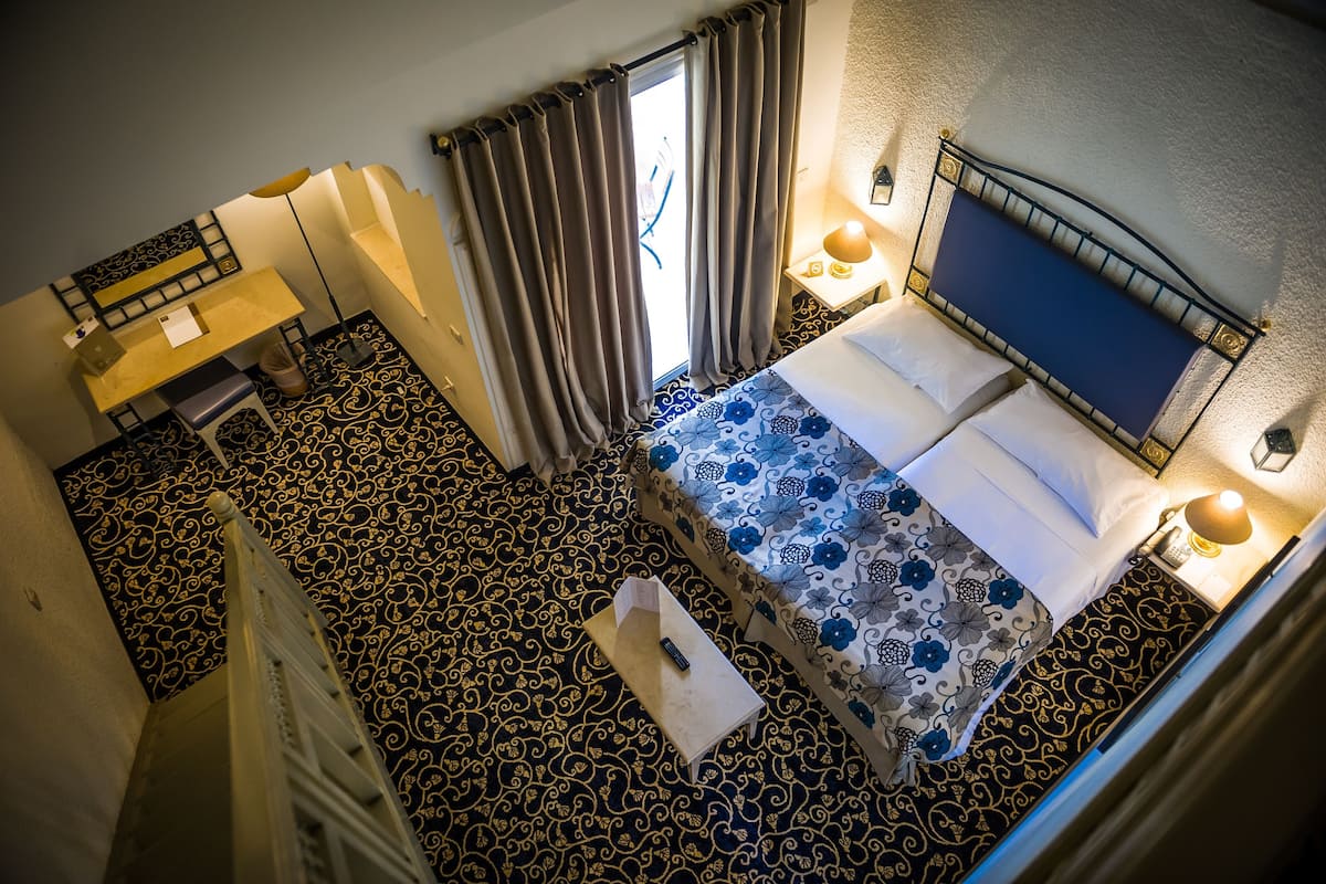 Habitación de hotel con cama, escritorio, silla, una mesita y una ventana con cortinas.