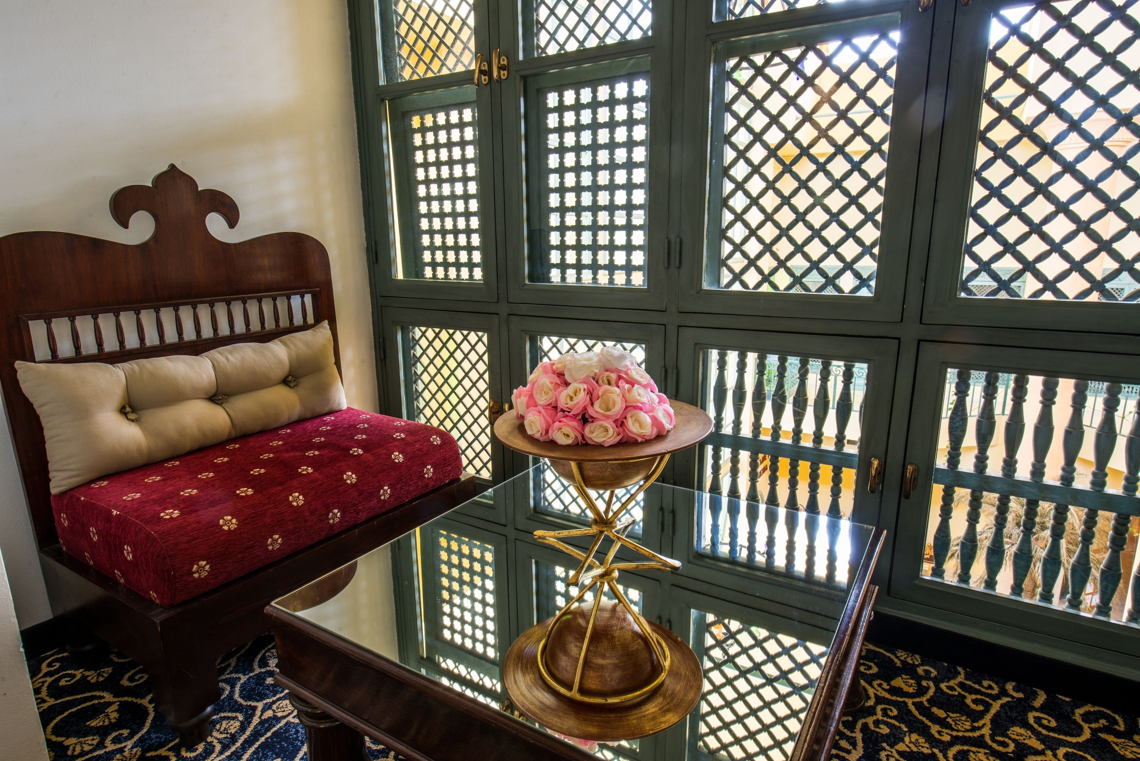 A room with a wooden headboard, a glass table with a decorative item, and a patterned floor.