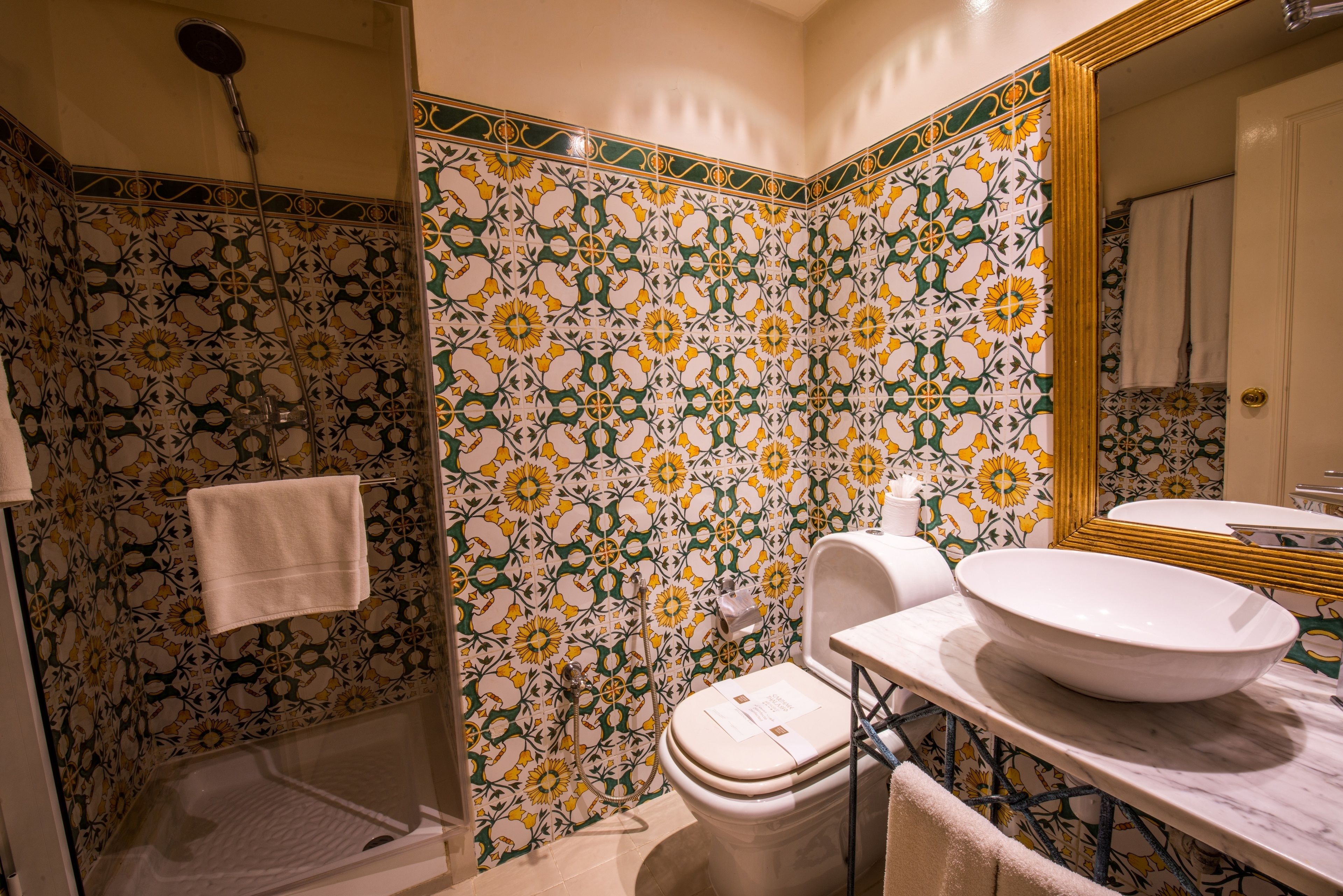 Un baño con lavamanos grande, inodoro y ducha. Las paredes están decoradas con un estampado floral de azulejos.