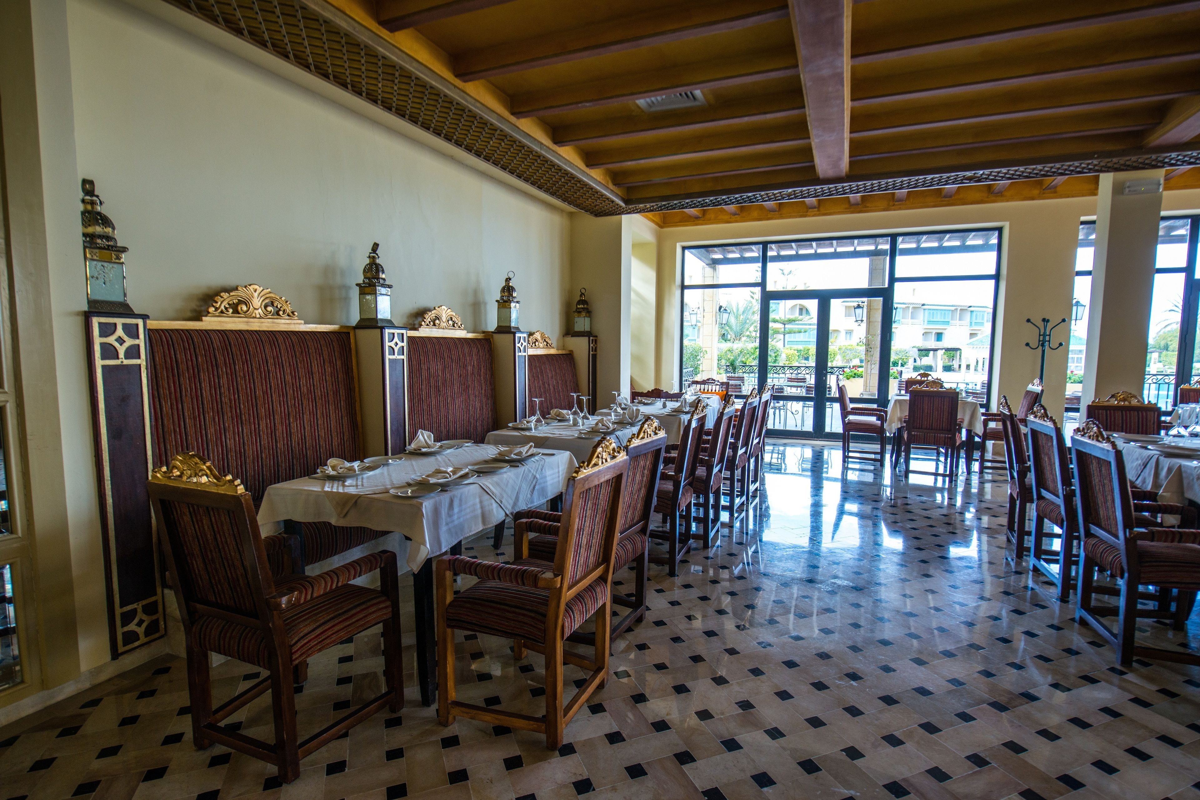A dining area with long tables, chairs, and decorative elements like wall-mounted sconces and a patterned floor.