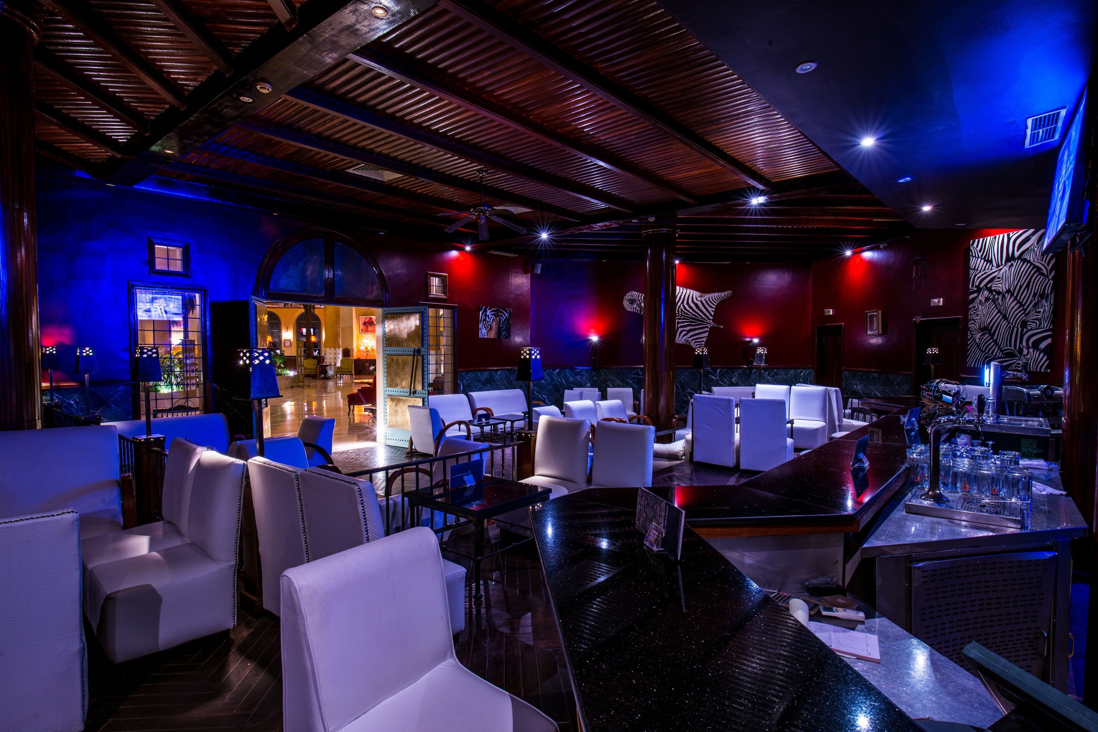 Un espace bar doté d’un comptoir en marbre noir, de sièges en cuir blanc et d’un éclairage d’ambiance aux couleurs rouge et bleu.