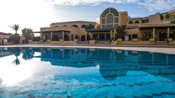 A pool area with a clear blue pool, a large arched window, and a building with multiple balconies and a covered patio.