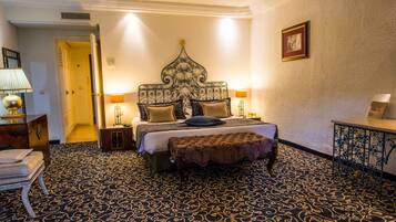 A hotel room with a large bed, a bedside table, a lamp, a picture frame, and a patterned carpet.