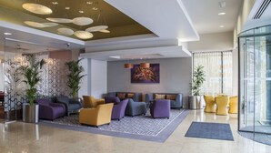 A modern lobby with a seating area, a patterned rug, and a large abstract painting on the wall.