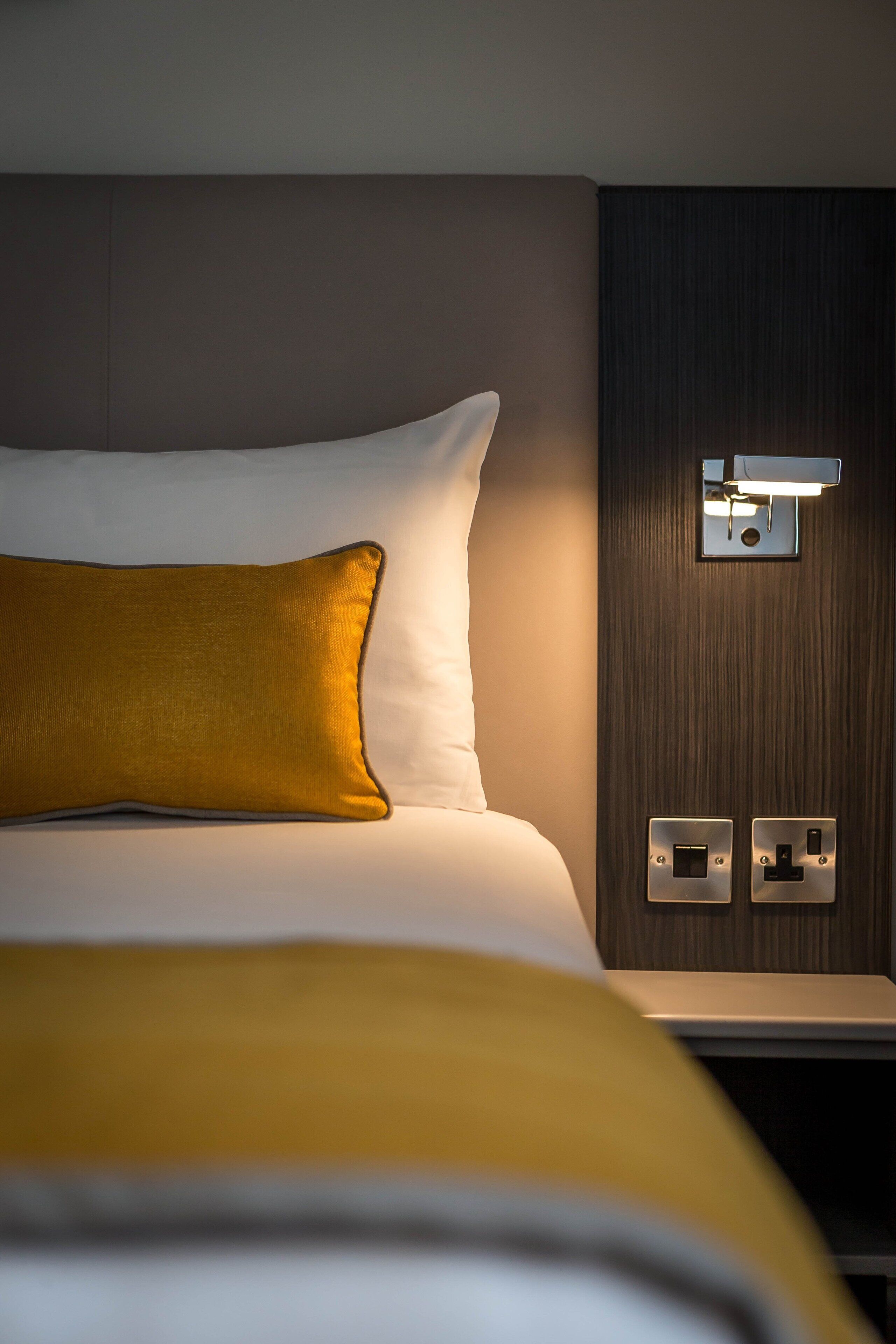 Une chambre d’hôtel avec un lit, une table de chevet et un luminaire fixé au mur.