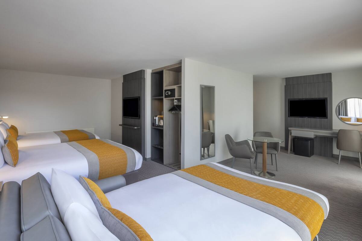 A hotel room with two beds, a desk, a chair, a TV, and a wardrobe.