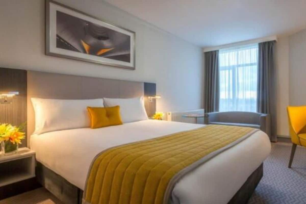 A hotel room with a large bed, a desk, a chair, and a window with curtains.