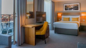 A hotel room with a bed, a desk with a chair, a television, and a window with curtains.