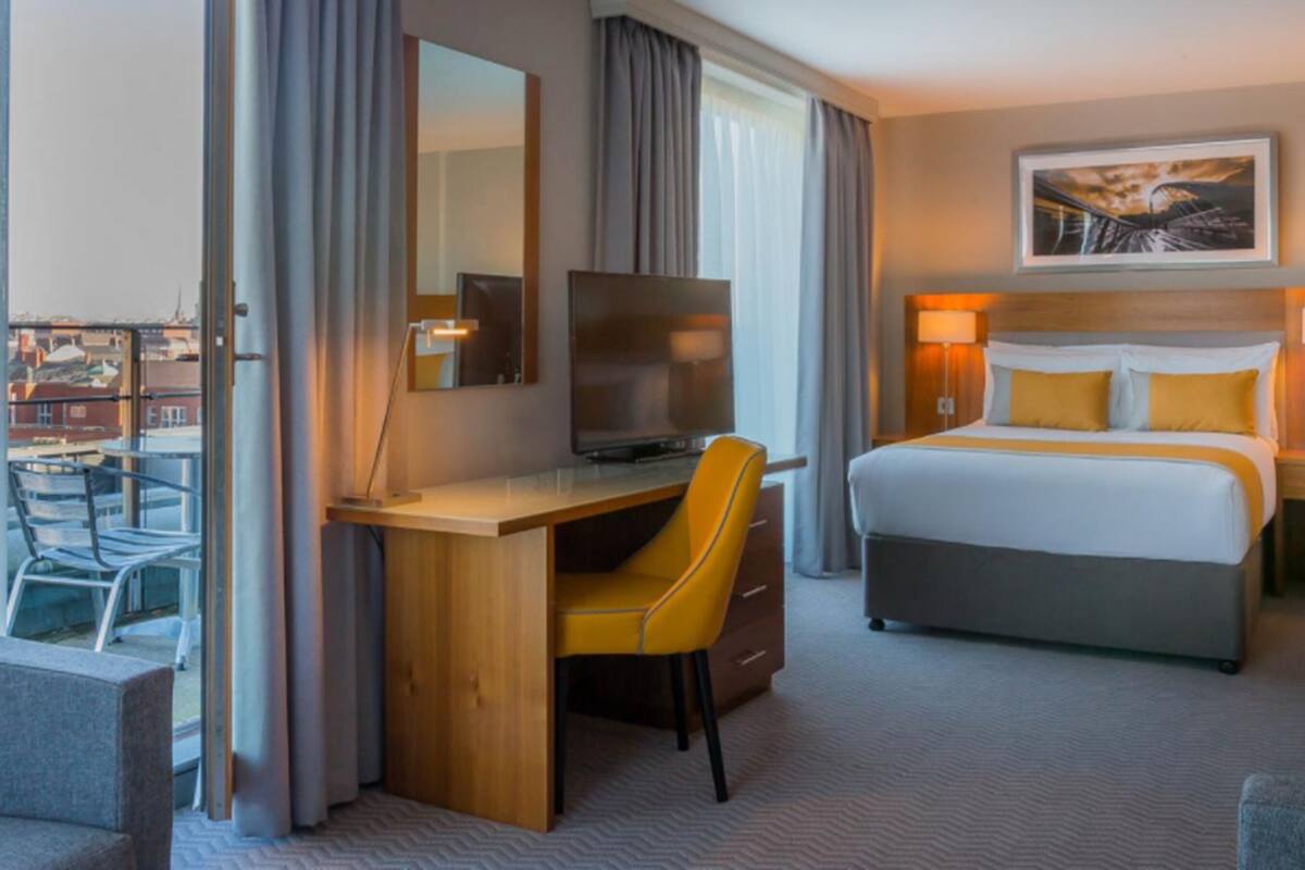 A hotel room with a bed, a desk with a chair, a television, and a window with curtains.
