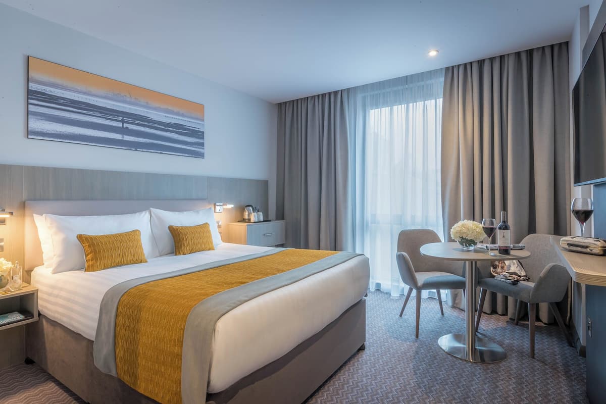 A hotel room with a large bed, a desk, and a TV.