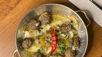 A bowl of meatballs in a sauce with vegetables and a red chili pepper on a wooden table.
