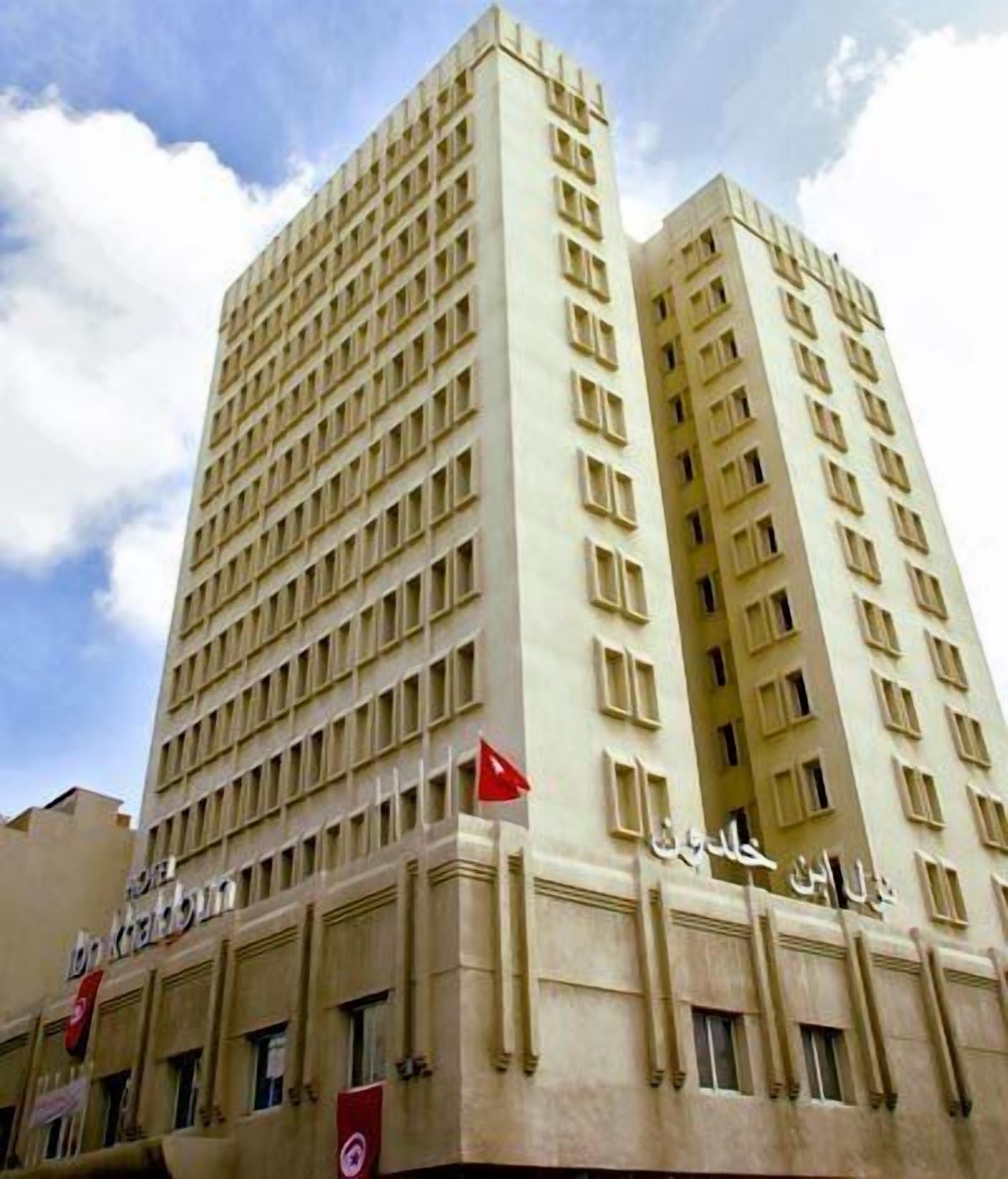 A tall, beige-colored hotel with multiple floors and a flag on top.