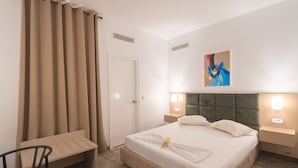 Una habitación de hotel con cama, mesitas de noche, una silla, un escritorio y un cuadro en la pared.
