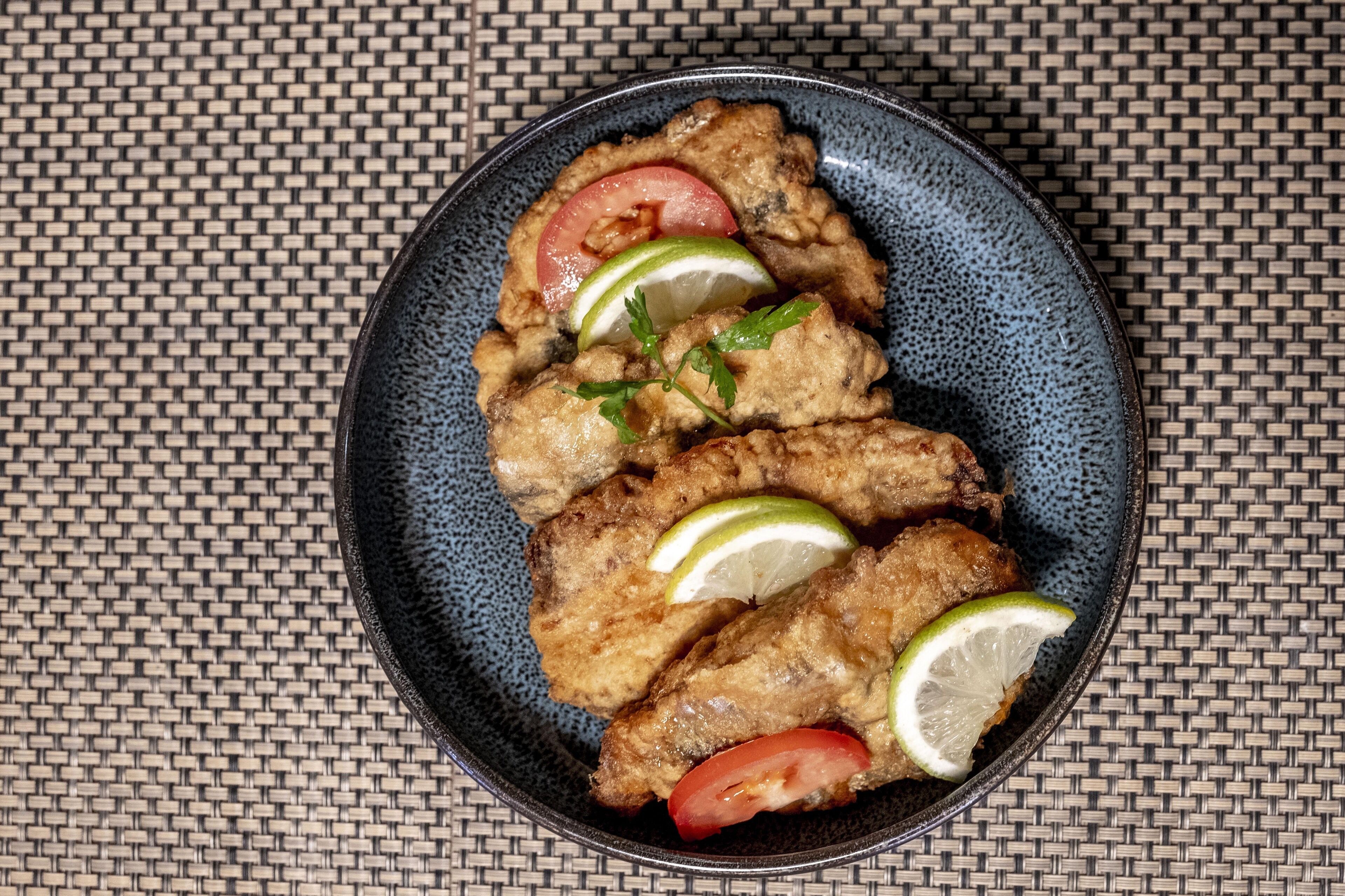 A plate of fried chicken with lime and tomato slices on a woven mat background.