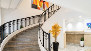 Una escalera curva con barandillas negras, una planta en maceta y un mostrador de recepción con encimera de madera.
