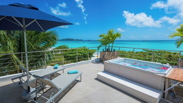 A balcony with a view of the ocean, a hot tub, and a table with chairs. - Acajou Beach Resort (Praslin Island)
