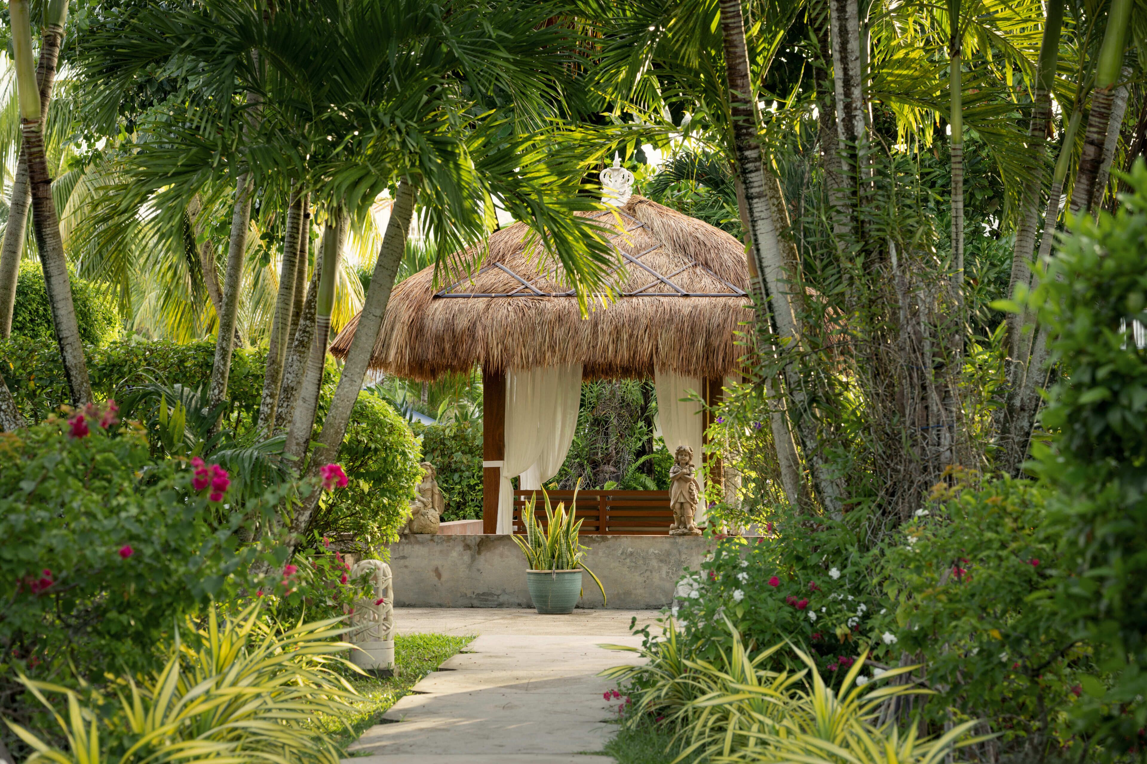 A thatched-roof structure surrounded by lush greenery and a pathway leading to it.