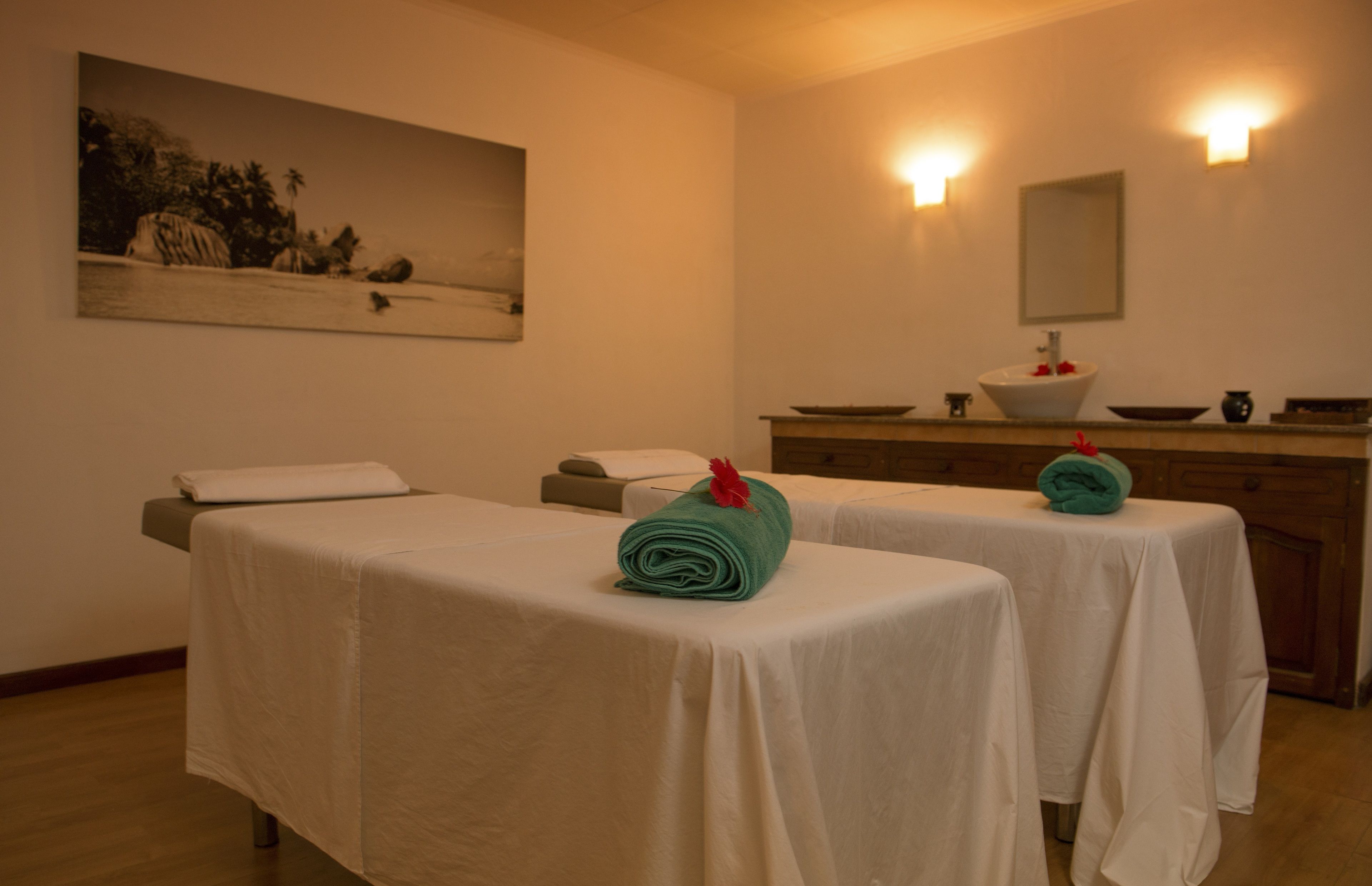 A spa room with two massage tables, a large painting, a sink, and a mirror.