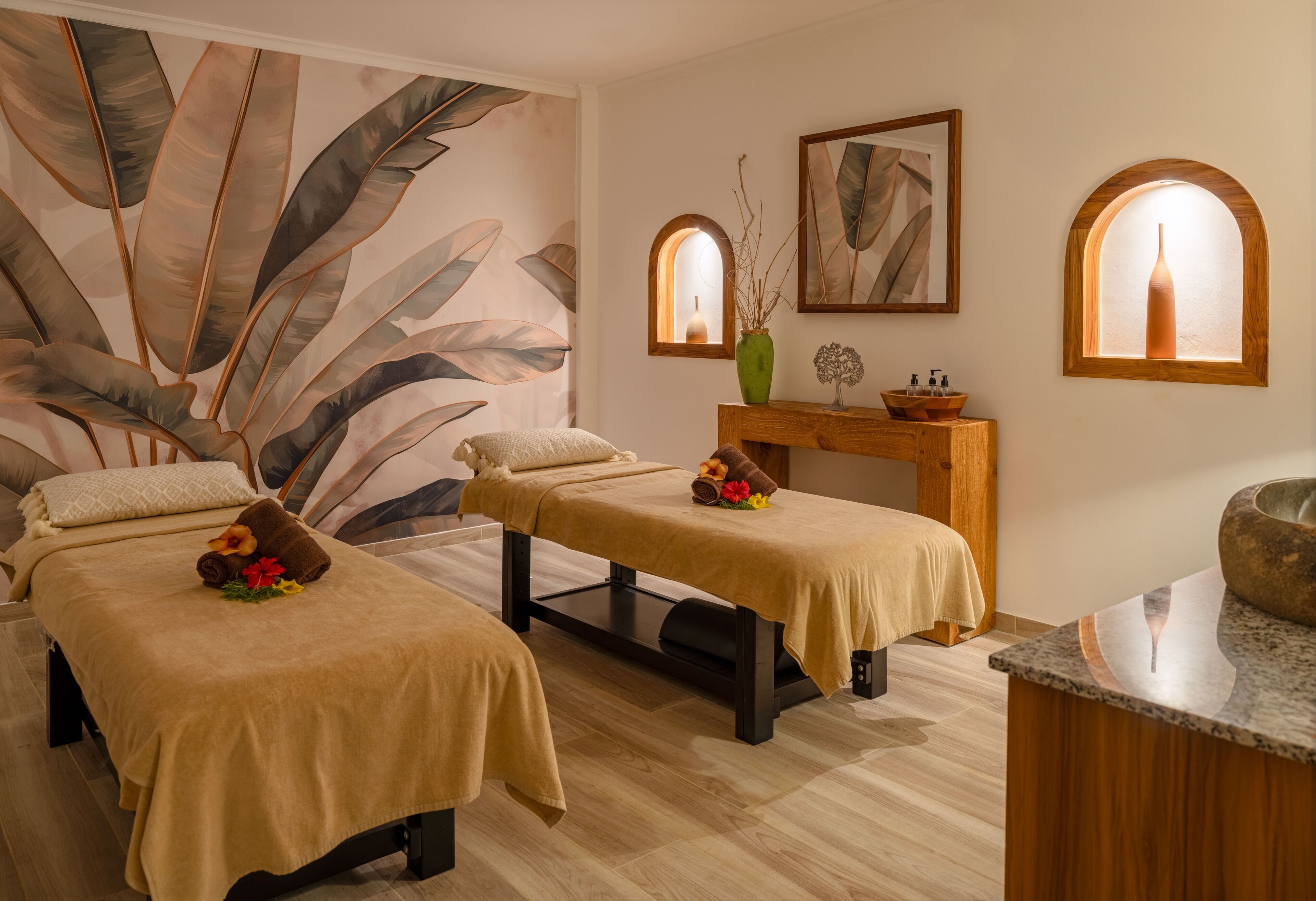 Un cuarto de spa con dos camillas de masaje, un banco de madera, un florero y una obra de arte enmarcada.