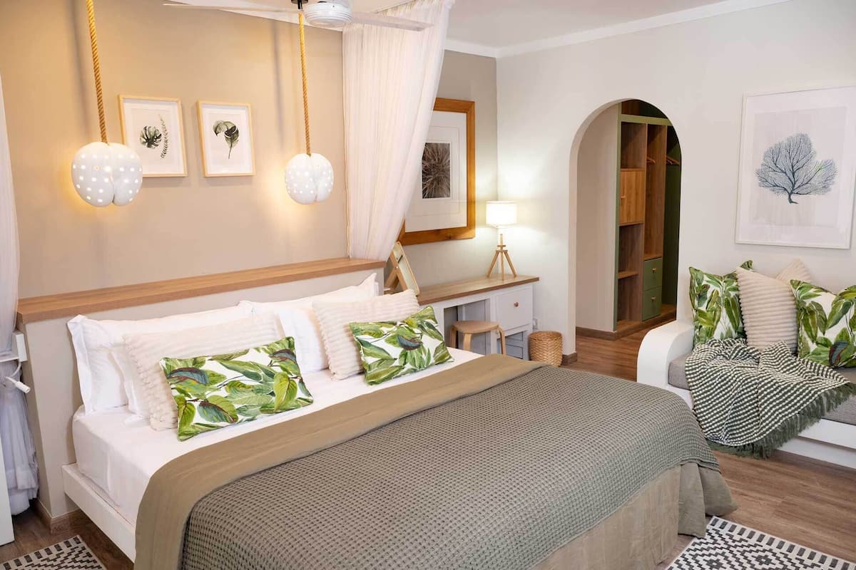 Une chambre à coucher comprenant un lit, une table de chevet, une lampe, une armoire et donnant sur le couloir.