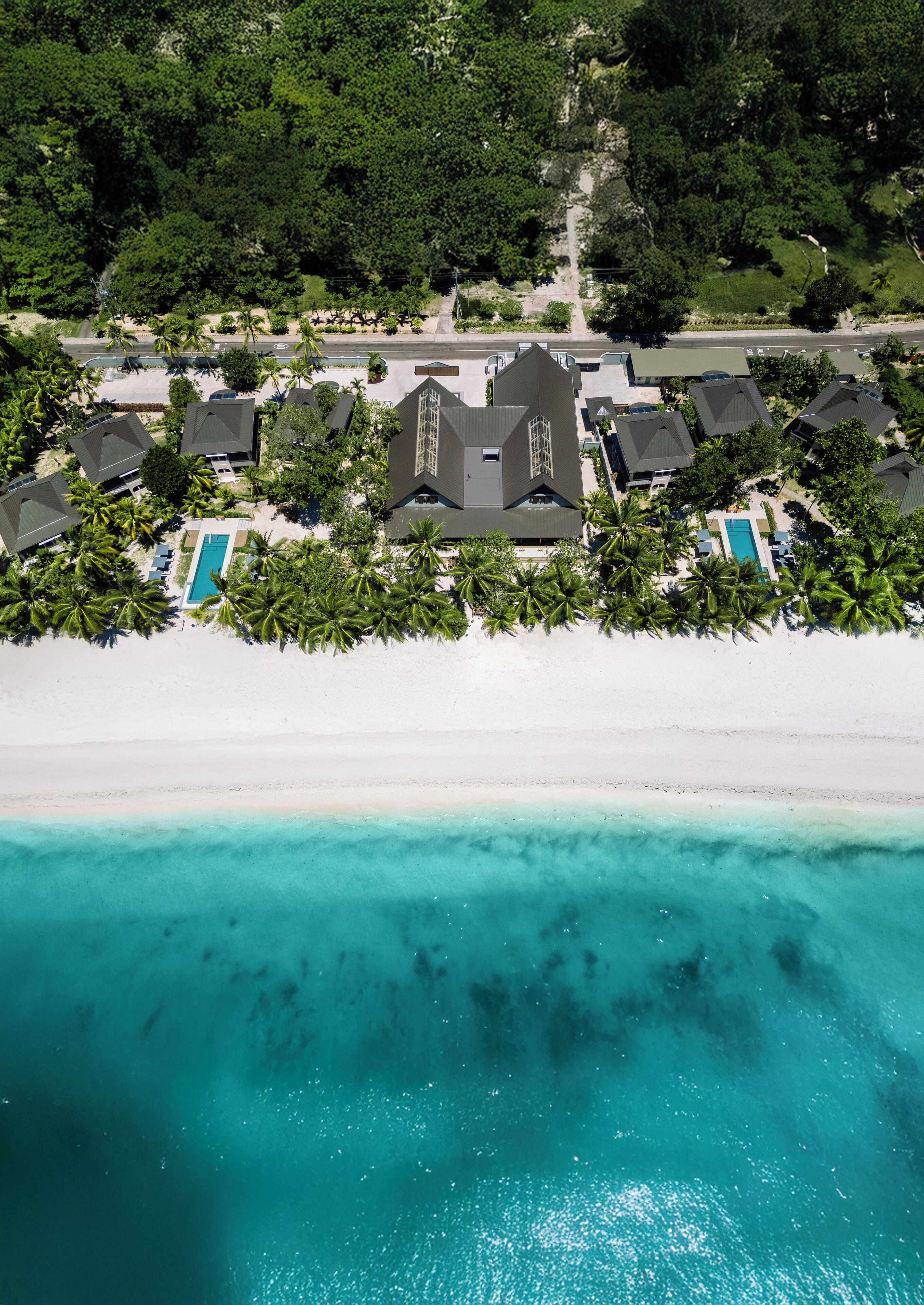 Vista aérea de um resort na praia com várias villas, uma piscina e uma praia de areia.