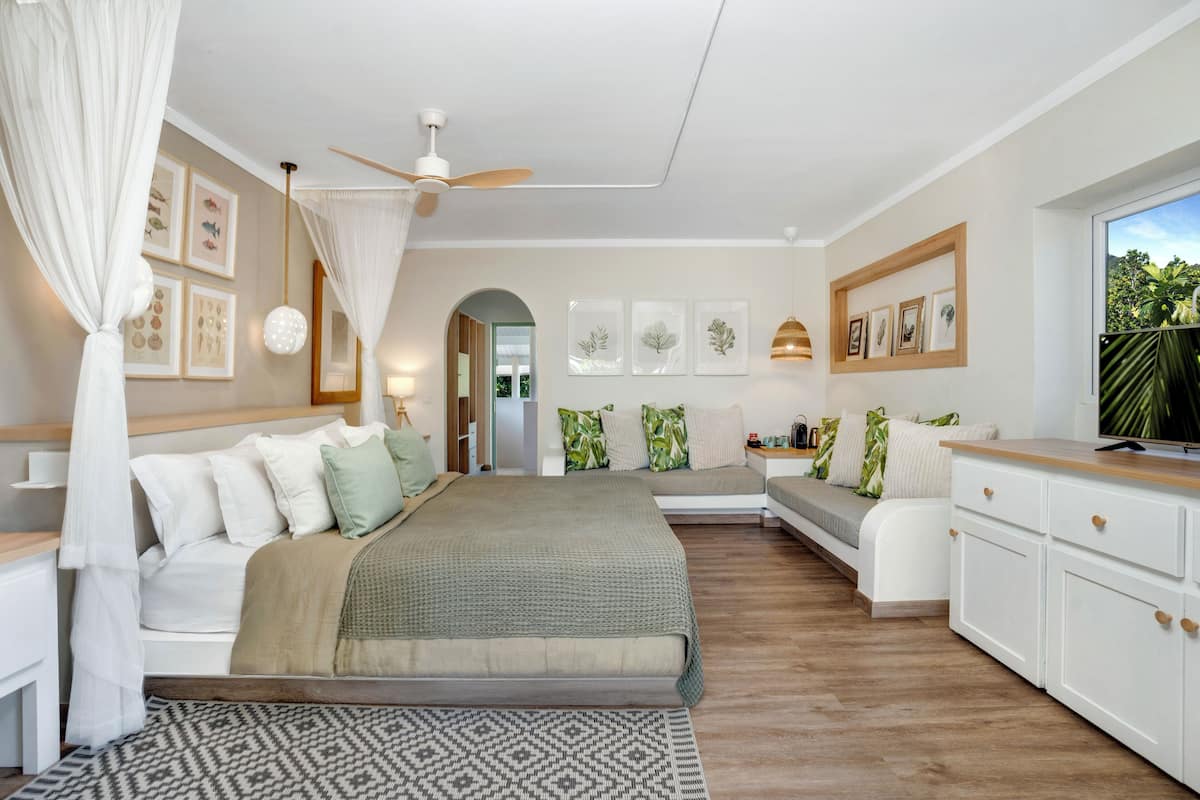 Une chambre à coucher comprenant un lit, des tables de chevet, une commode, une fenêtre avec vue, un ventilateur de plafond et des œuvres d’art accrochées au mur.