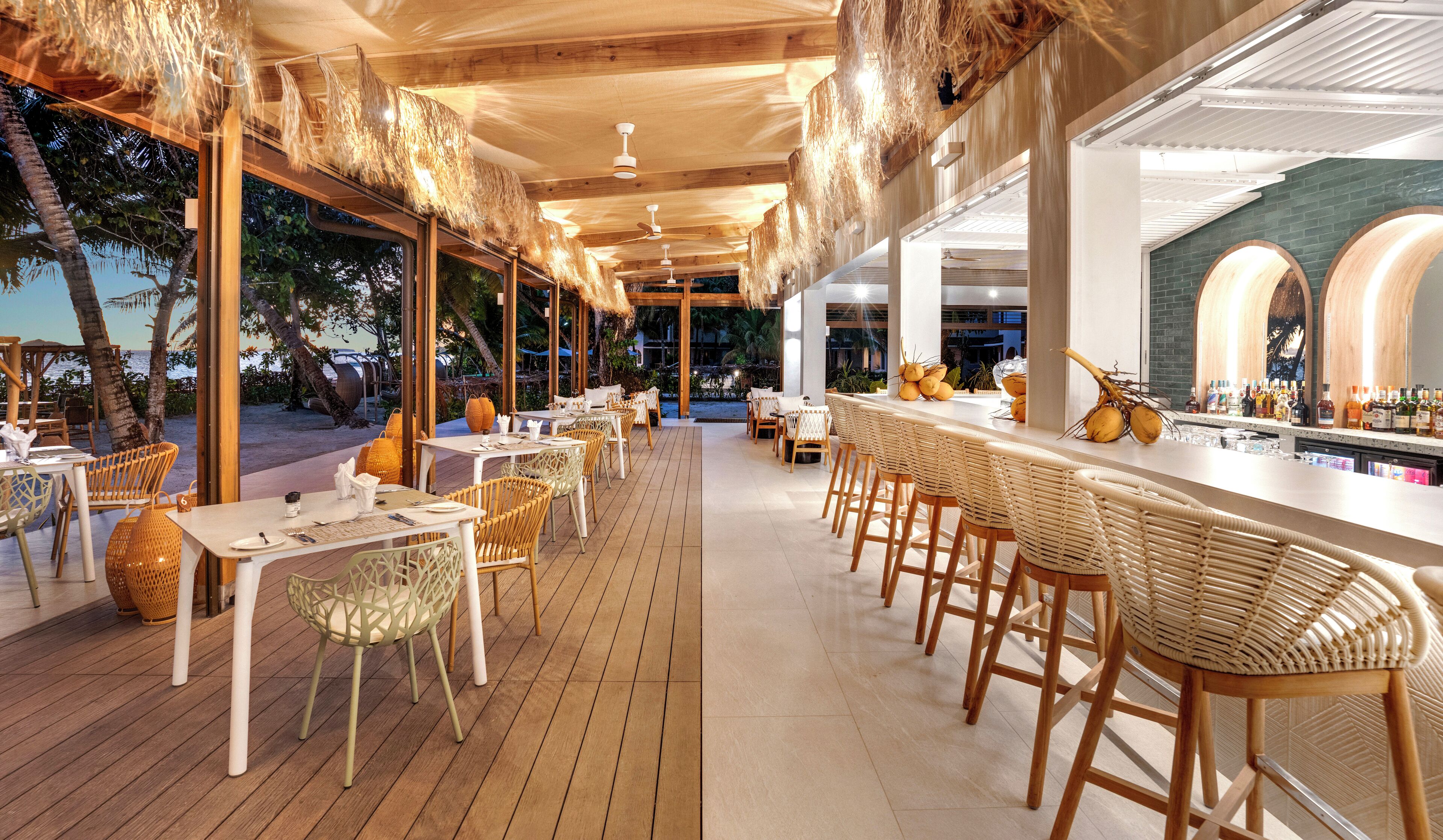 A restaurant with outdoor seating, wooden tables, wicker chairs, and a bar area with bottles.