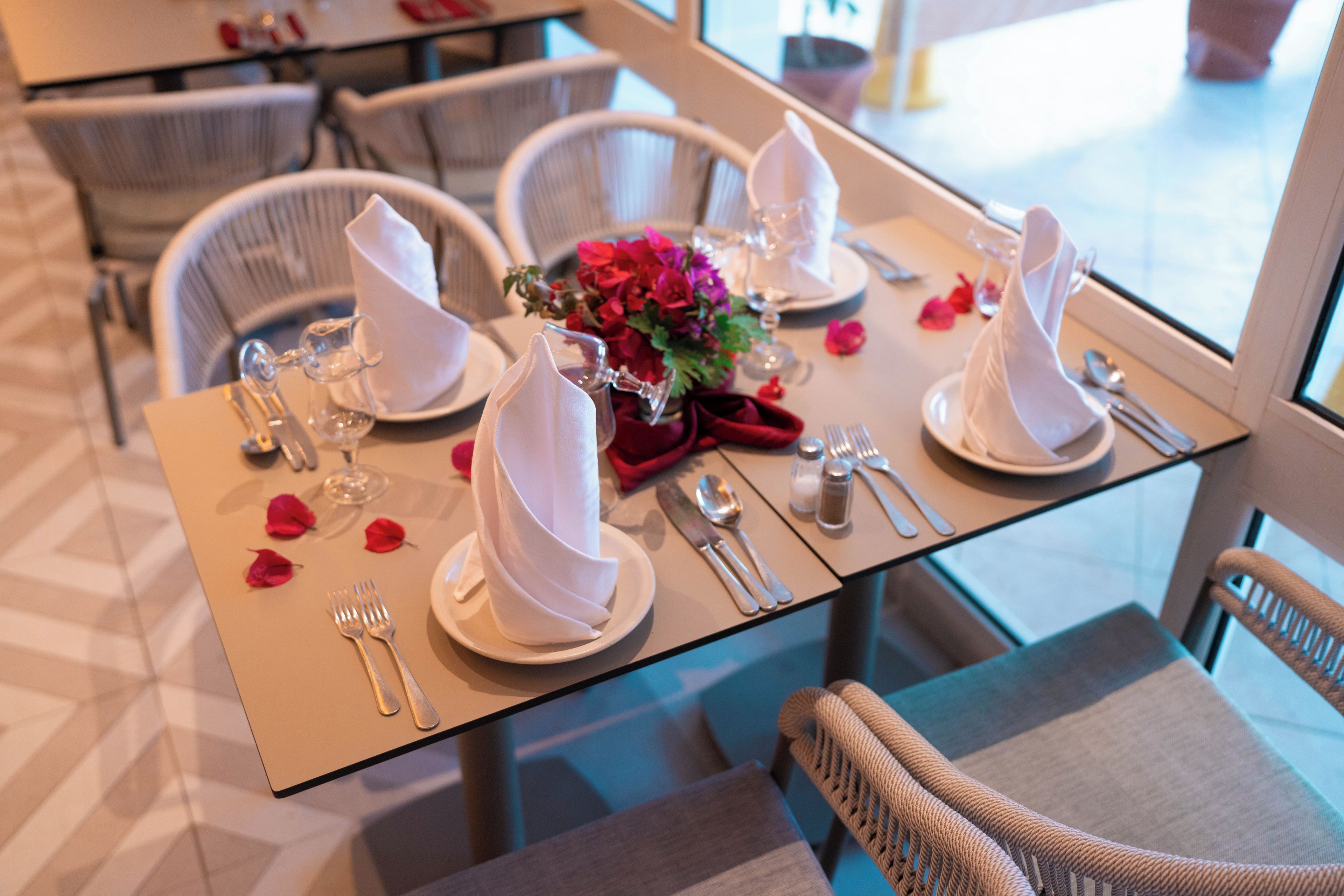 A dining table set with white napkins, silverware, and a vase of flowers.