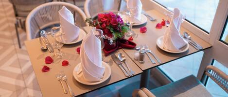 A dining table set with white napkins, silverware, and a vase of flowers.