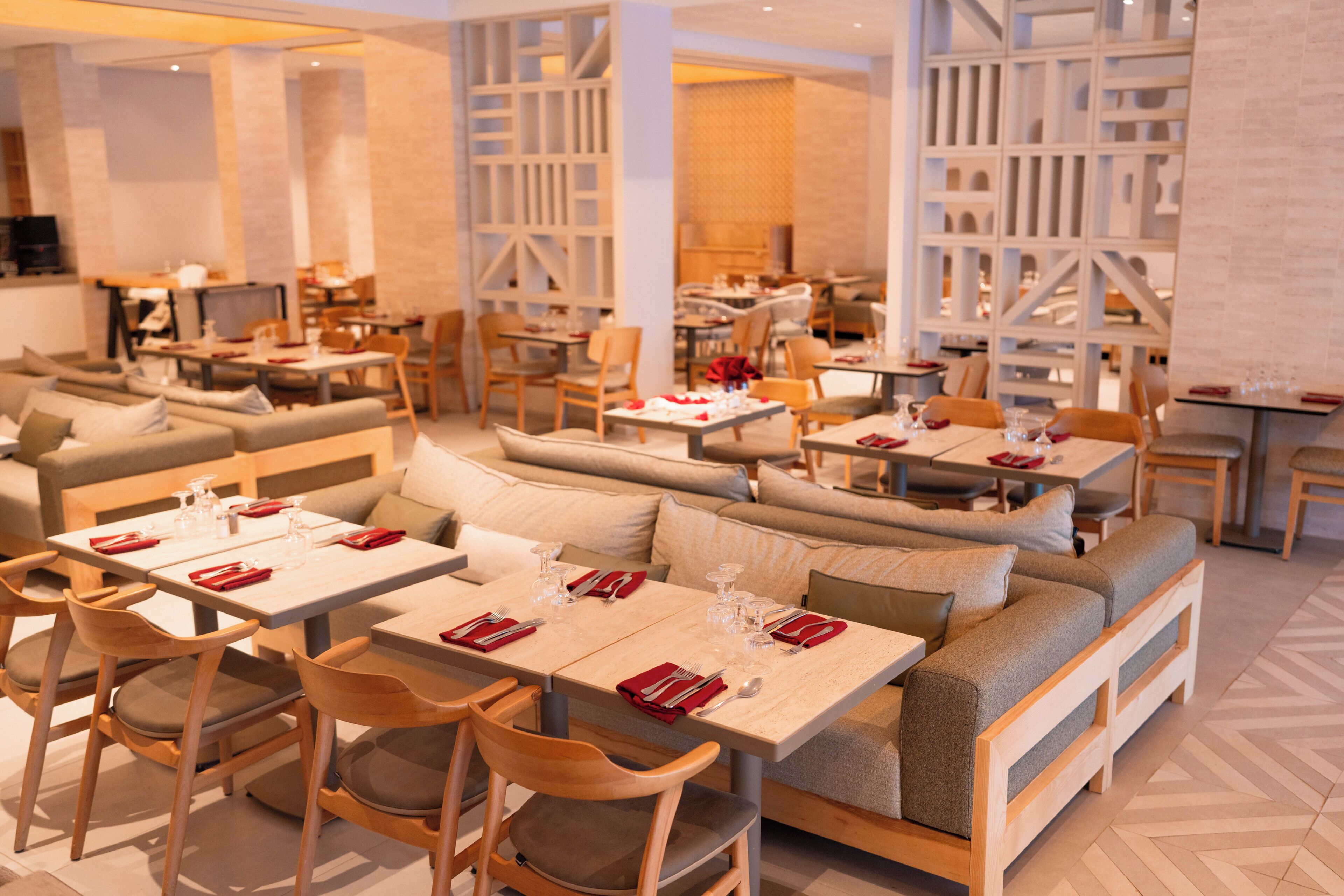 Un restaurant moderne doté de plusieurs espaces de restauration, notamment des banquettes et des tables, chacune agrémentée de serviettes et de couverts rouges.