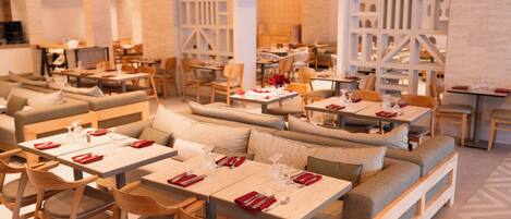 Un restaurant moderne doté de plusieurs espaces de restauration, notamment des banquettes et des tables, chacune agrémentée de serviettes et de couverts rouges.