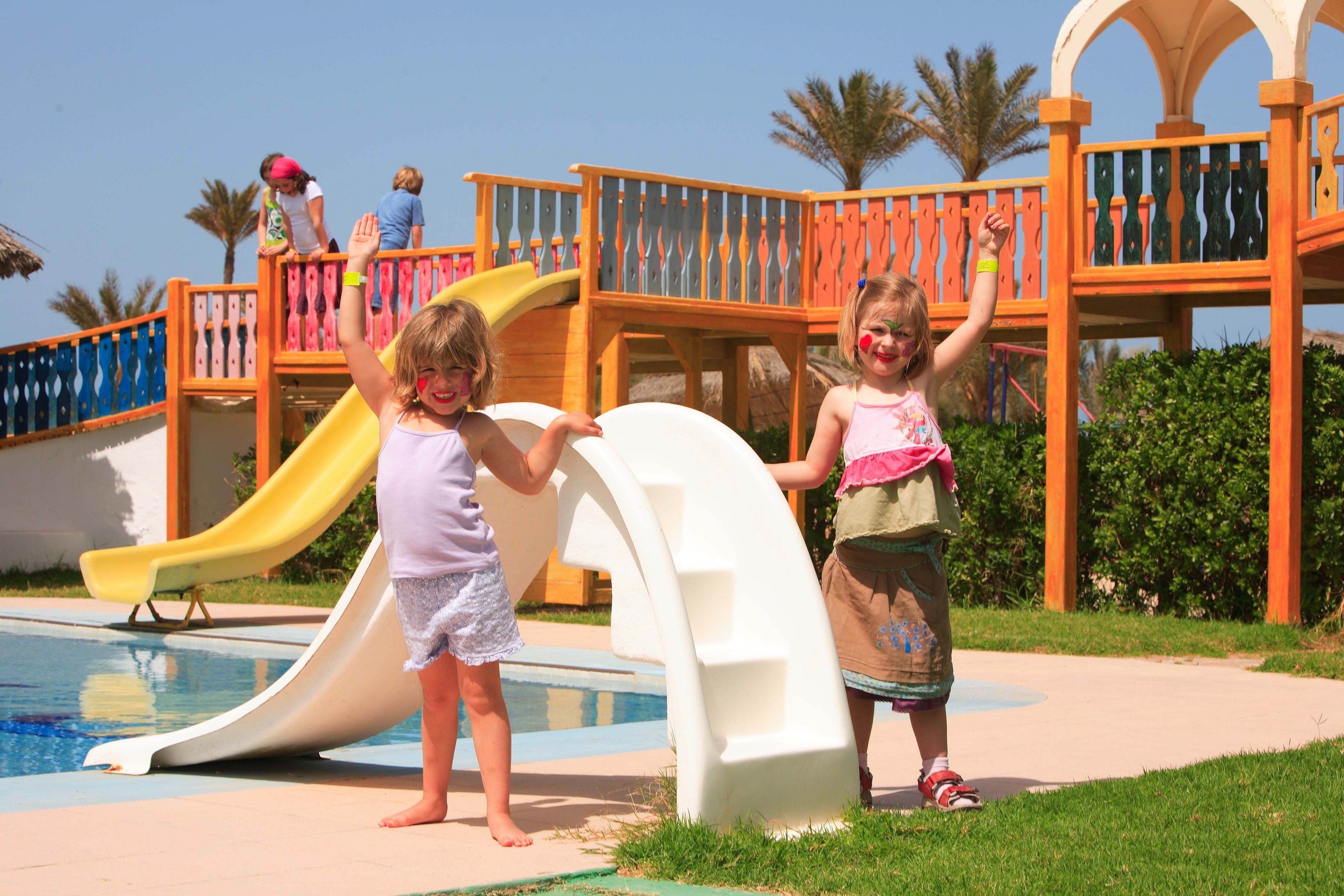 Children playing near a pool with a slide and a play structure.