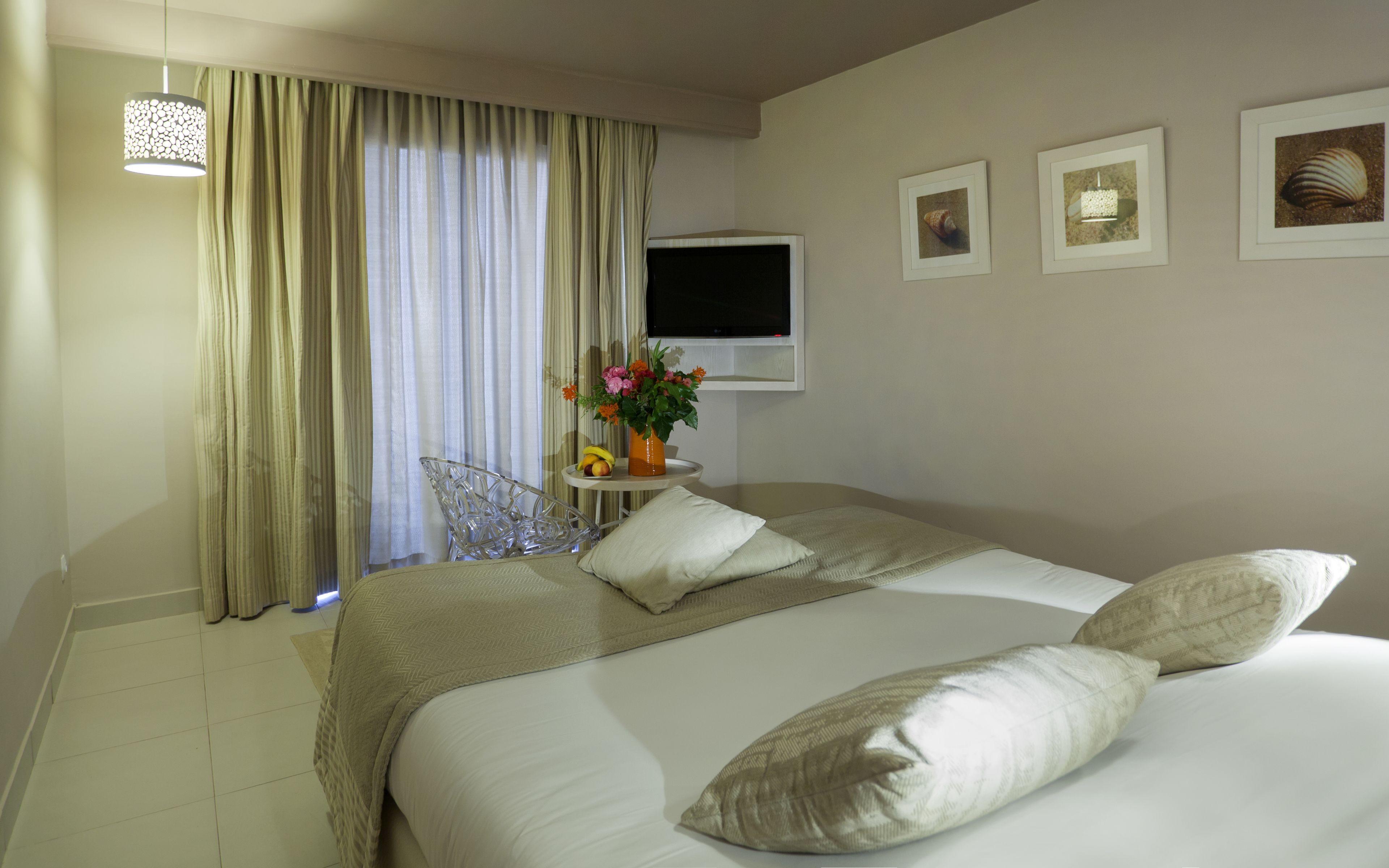A hotel room with a large bed, a TV, a chair, and a small table with a vase of flowers.